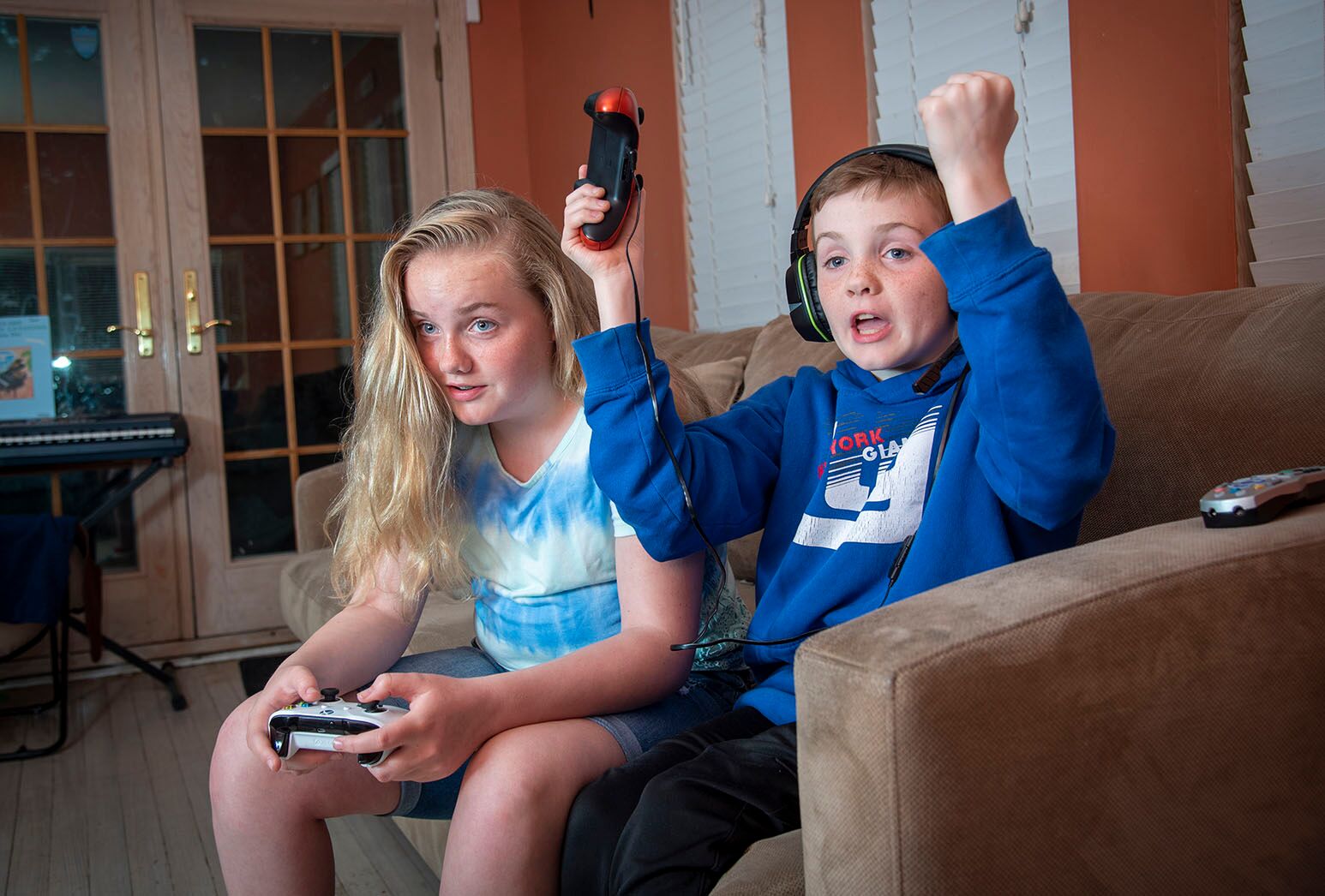 Young girl with long blond hair and boy with dark hair and headphones playing a video game on couch.